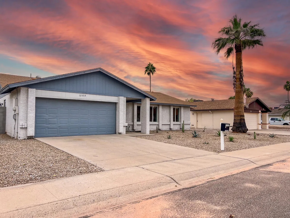 A wide exterior shot of the house facade at sunset, framed by palm trees and a welcoming entrance. The garage and driveway are visible, suggesting easy access and a quintessential Arizona suburban setting. The sky glows with warm sunset colors, reinforcing the outdoor, leisure-focused lifestyle.