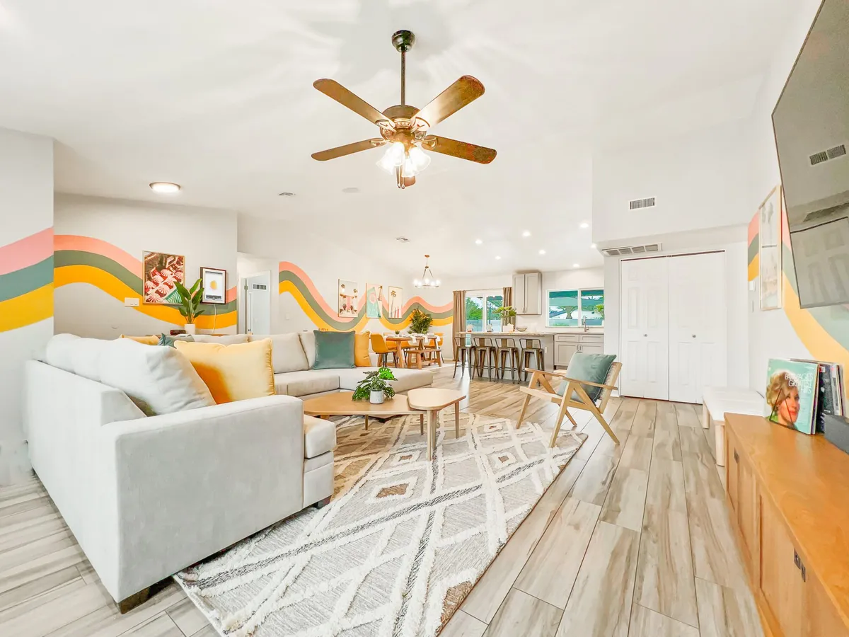An inviting open-plan space blending the large sectional sofa, wooden dining table, pops of color from a striking wall design, and large windows looking out to the pool and backyard. The layout fosters seamless interaction between lounging, dining, and enjoying the view.