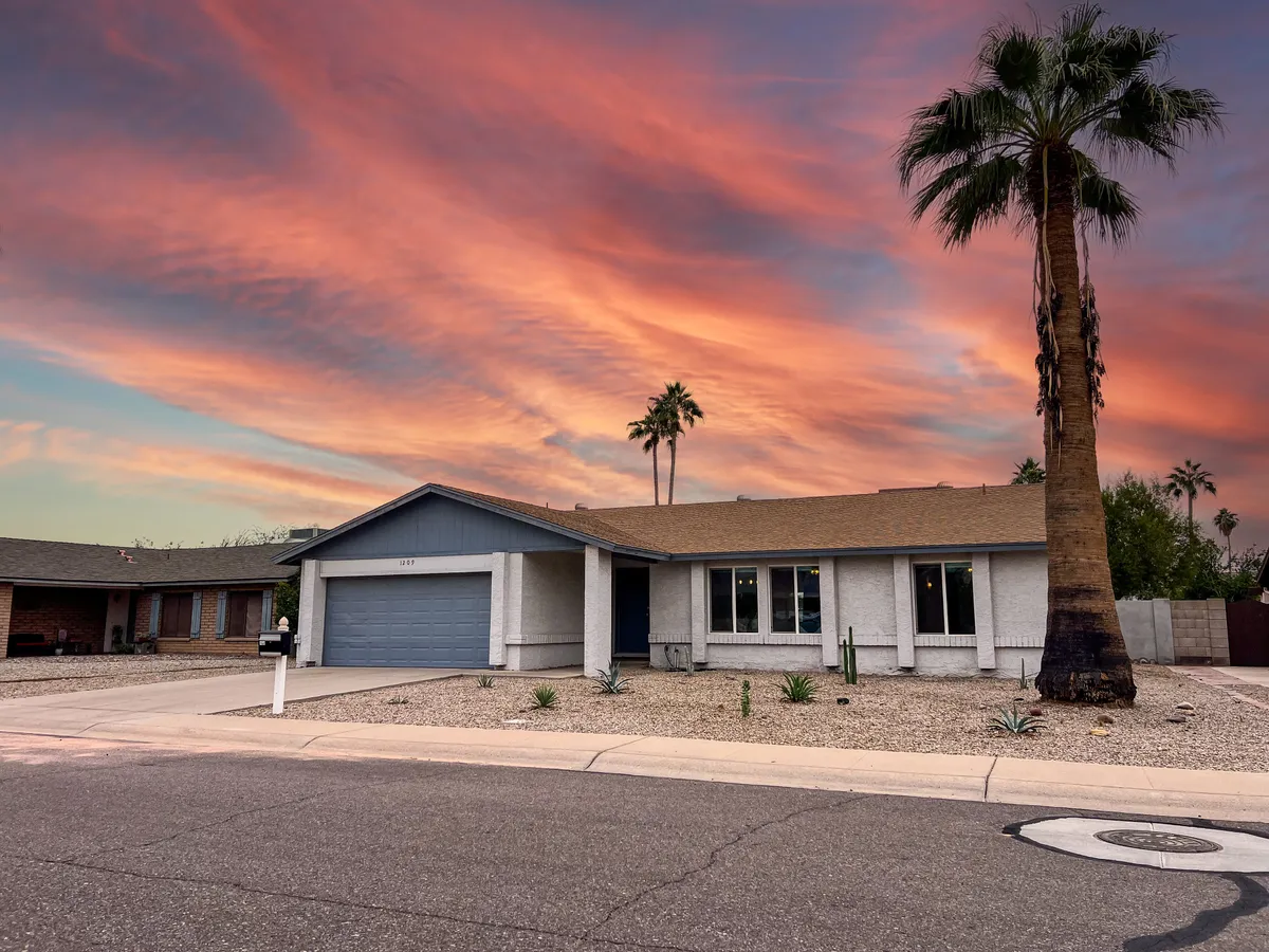 This image features the house's exterior framed by tall palm trees and a vibrant sunset sky, conveying a warm and inviting atmosphere. The landscaped yard and front porch suggest a connection to the outdoors, perfect for relaxing after a day exploring the city.
