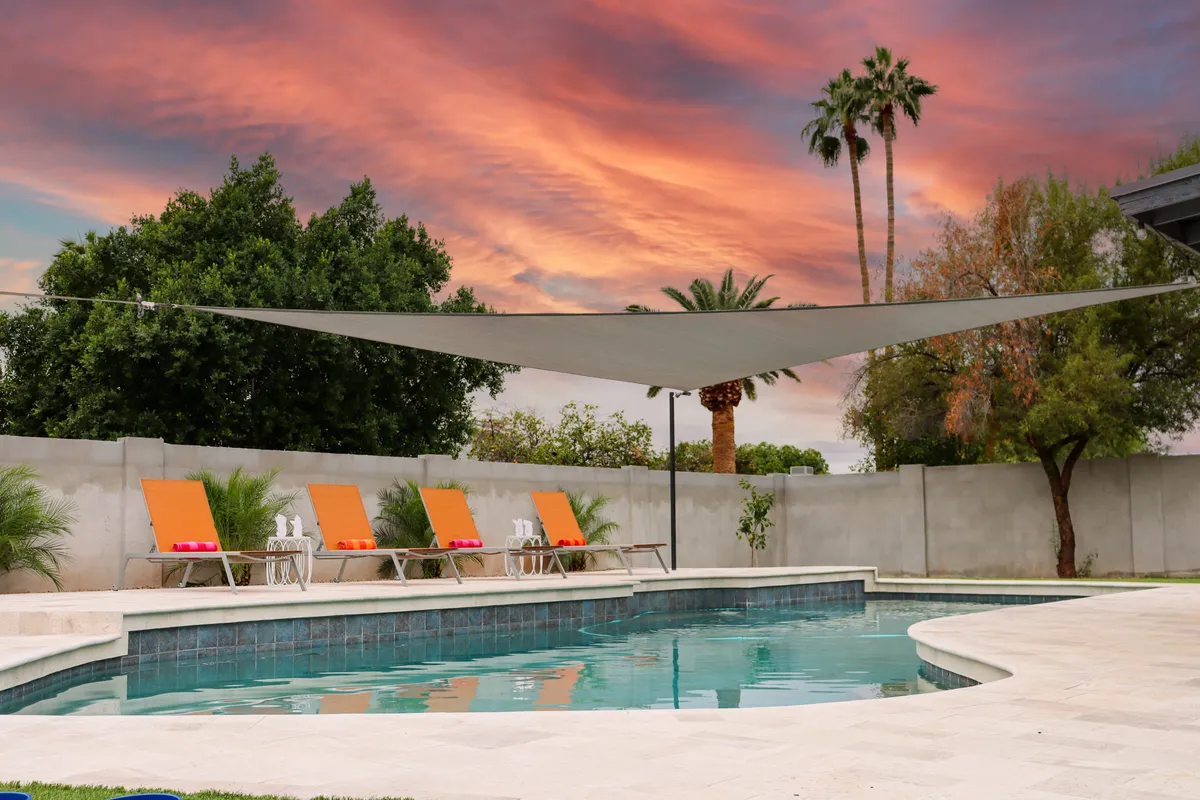 A tranquil scene showcasing a sparkling swimming pool surrounded by lounge chairs and tall palm trees under a colorful sunset. The inviting layout is ideal for relaxation, sunbathing, or gathering with friends after a day on the fairways.