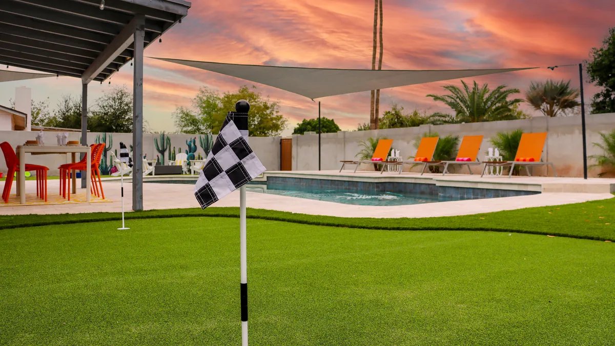 This playful exterior shot features a putting green adjacent to the swimming pool, with colorful chairs for lounging and a beautiful sunset sky in the background. The image captures the dual leisure options of golf and pool fun, with vibrant colors contributing to an inviting, vacation-like mood.