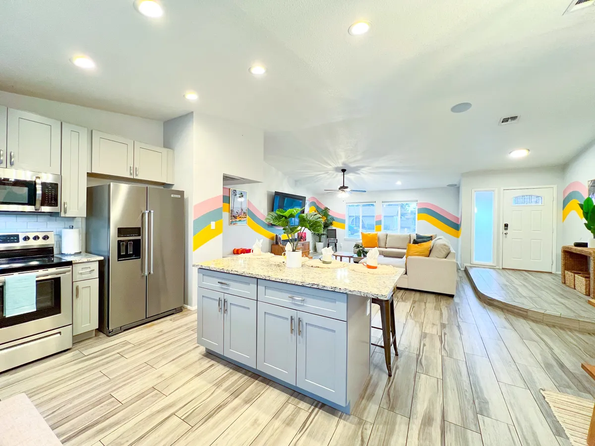 A vibrant kitchen and adjacent living space are featured, with a contemporary kitchen island, modern appliances, stylish wall art, and a glimpse of a cozy seating area. The setup suggests a flow between the kitchen and other gathering spaces, ideal for entertaining and family meals.